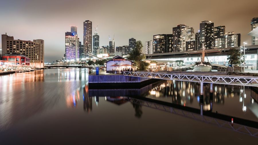 Reflection of illuminated buildings in river against sky