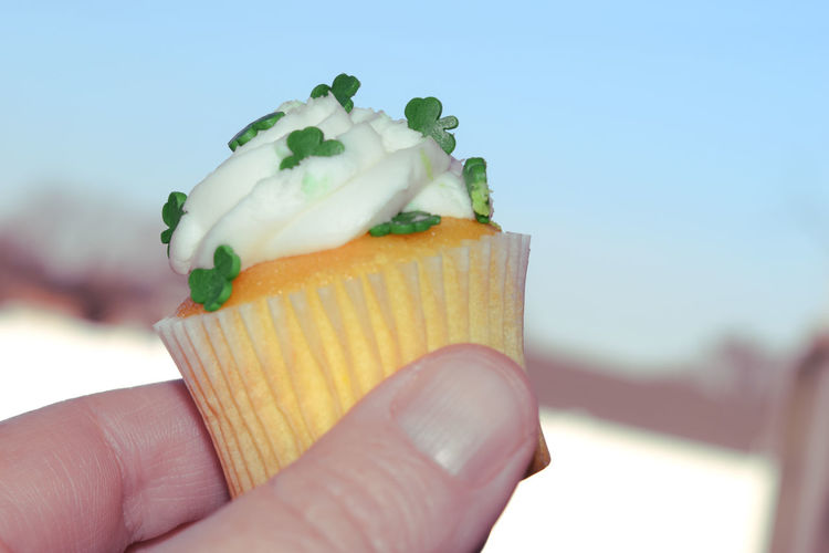 Close-up of hand holding cup cake against clear sky