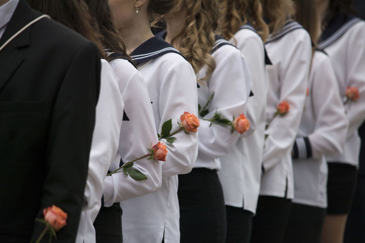 Midsection of women wearing uniform while standing in line with orange roses
