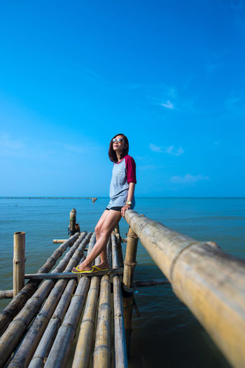 Woman standing on bamboo jetty against blue sky