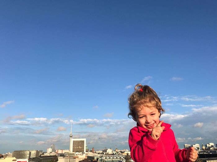 Portrait of smiling cute girl against cityscape