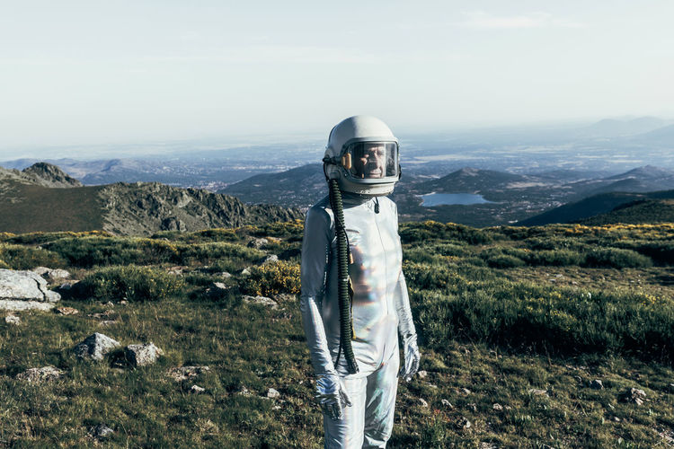 Male astronaut in spacesuit and helmet standing on grass and stones in highlands