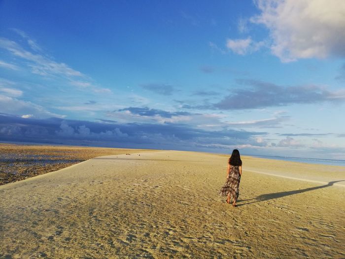 Rear view of woman walking at beach against sky  sandbar island  lowtide season 