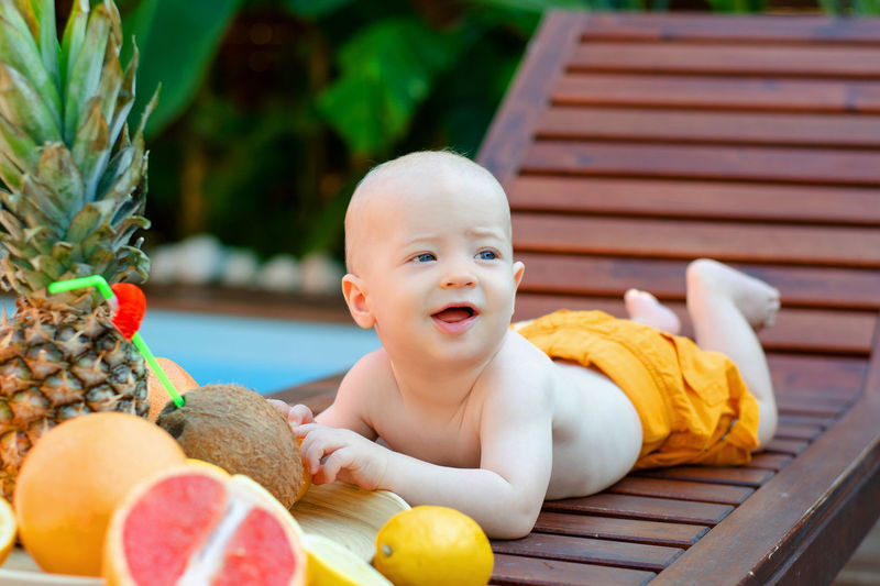 Cute baby boy looking away while lying on chair by fruits