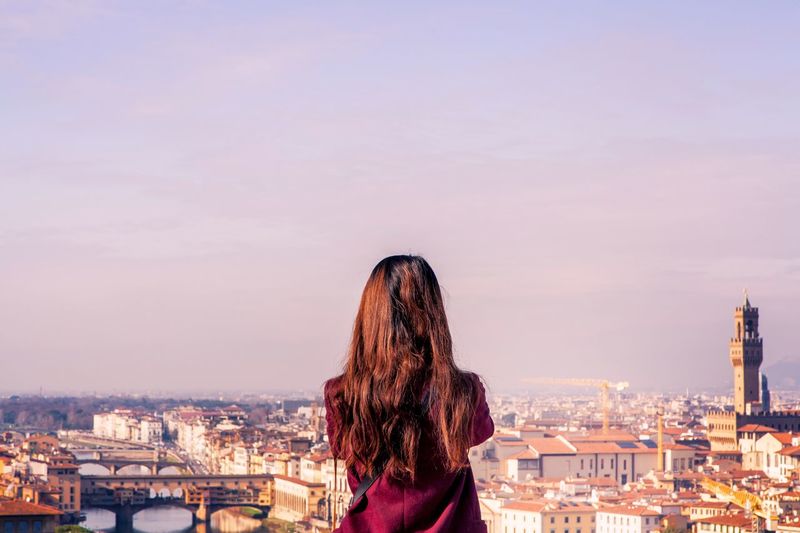 Rear view of young woman standing against cityscape during sunset