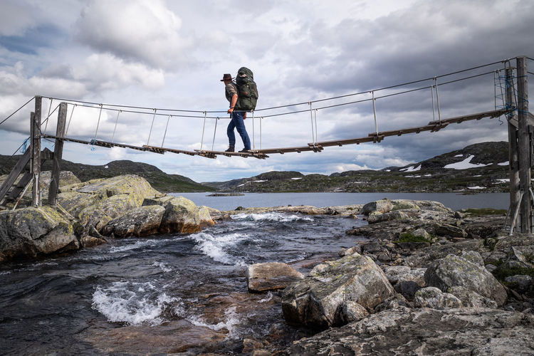 People on rock by bridge against sky