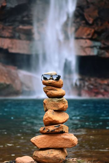 Close-up of sunglasses on stacked rock against waterfall