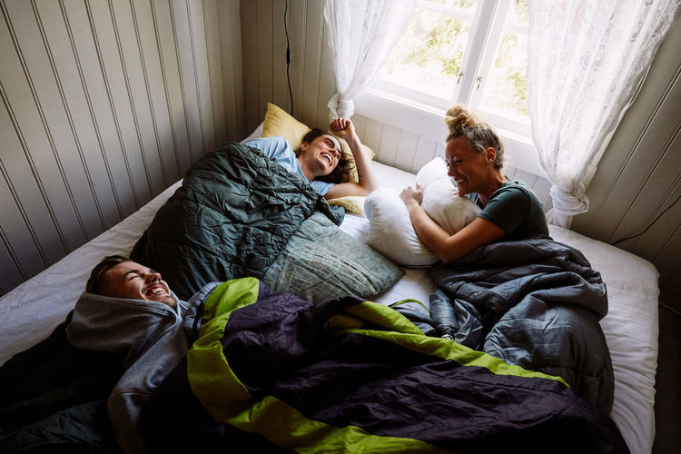 High angle view of cheerful male and female friends talking while lying on bed in cottage