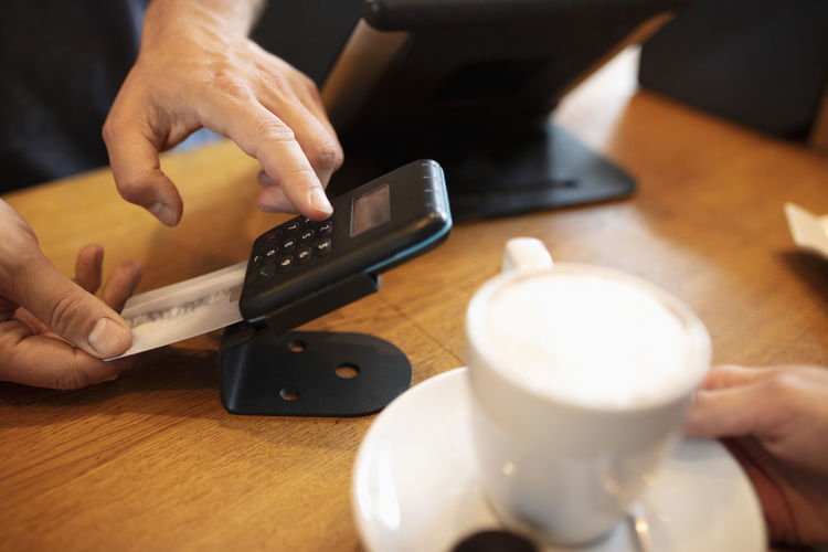 Hands of cashier using card machine at cafe counter