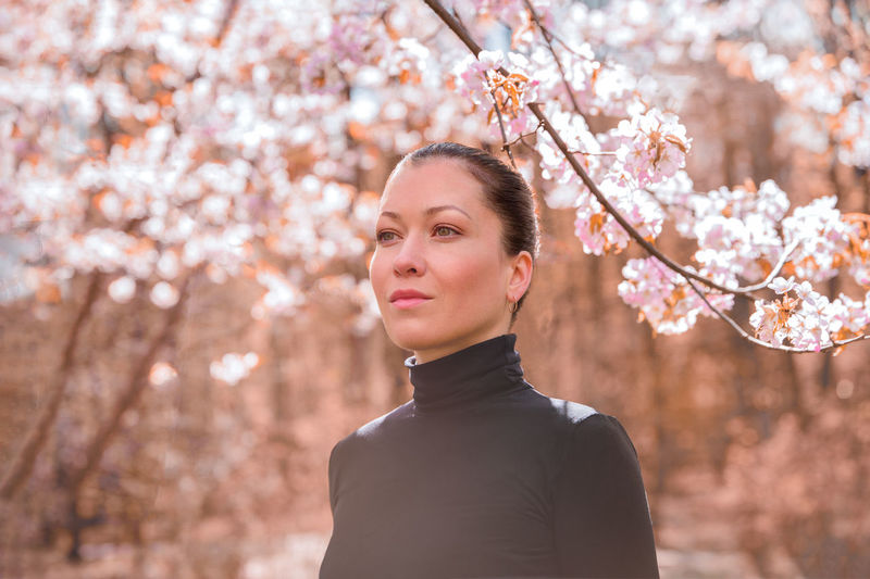 Portrait of young woman standing by cherry blossom tree