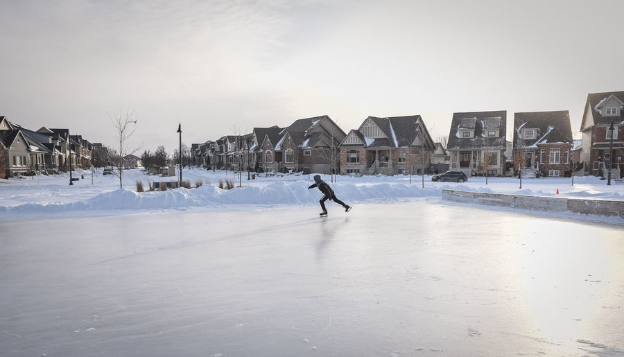 Boy skating fast on an empty outdoor neighbourhood ice rink.