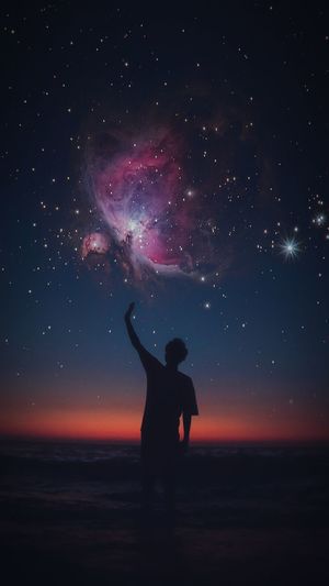 Silhouette man with hand raised standing at beach against star field
