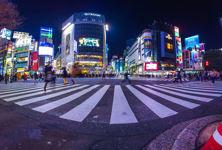 People crossing road in city at night at shibuya crossing , tokyo , japan