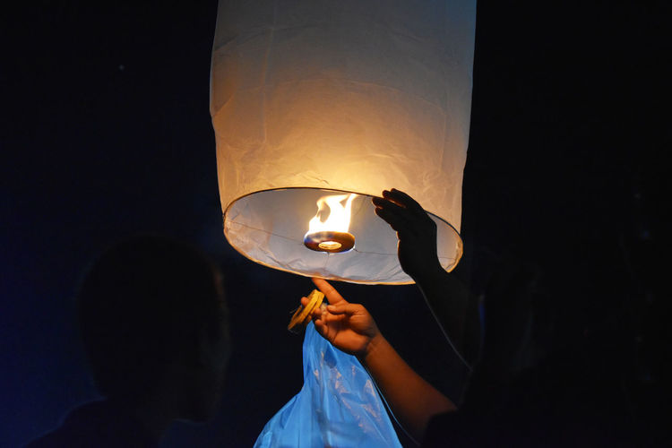 Friends igniting paper lantern at night