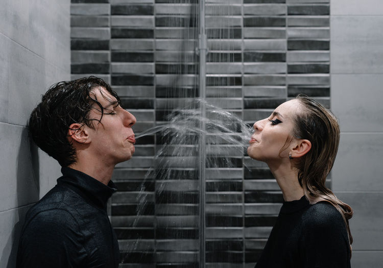 Young couple spitting water at each other in shower