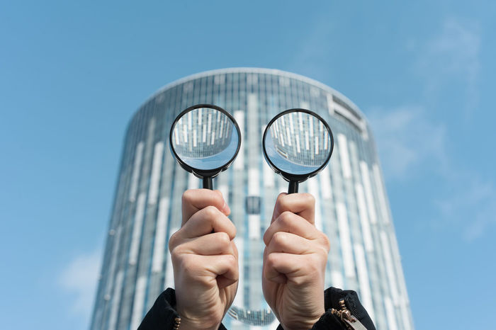 Close-up of hand holding magnifying glass against building