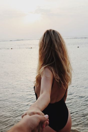 Woman holding cropped hand against sea during sunset