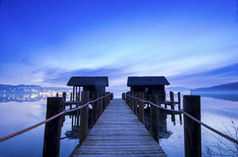 Wooden pier over lake against dramatic sky at dusk