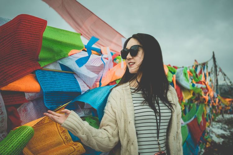 Woman in sunglasses standing against multi colored prayer flags