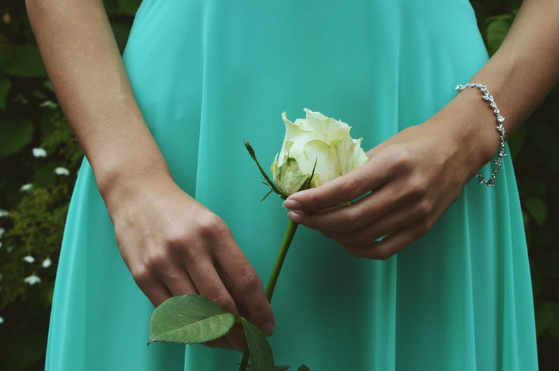 Midsection of woman in blue dress holding rose