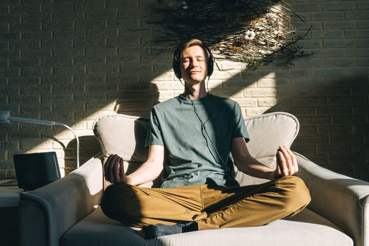 Full length of man meditating on sofa at home