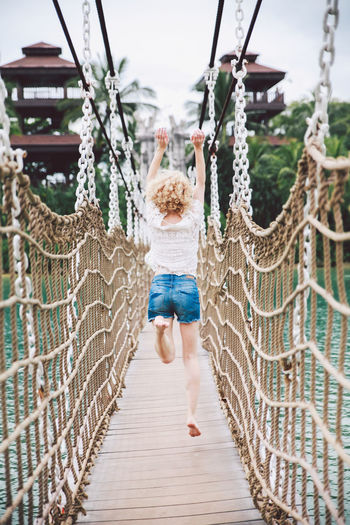 Rear view of young woman jumping over footbridge
