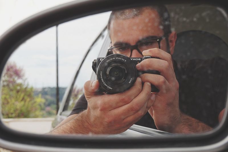 Reflection of man photographing with camera on side-view mirror of car