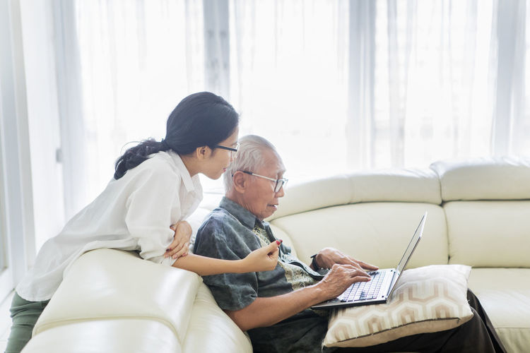 Grandchild teaching grandfather to use laptop