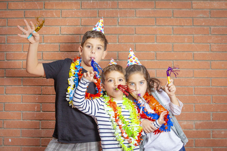 Portrait of siblings wearing garlands and party hats against brick wall