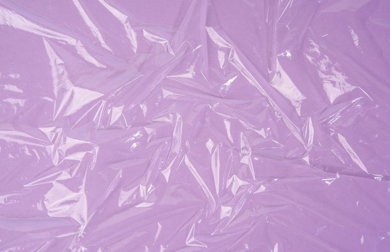 Texture of crumpled transparent polyethylene on purple background, full frame