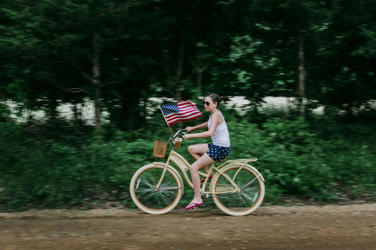 Girl riding her bike with an american flag on a rural dirt road