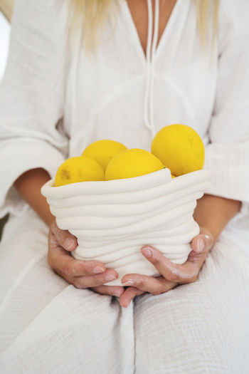 Woman wearing a white dress holding bowl with lemons