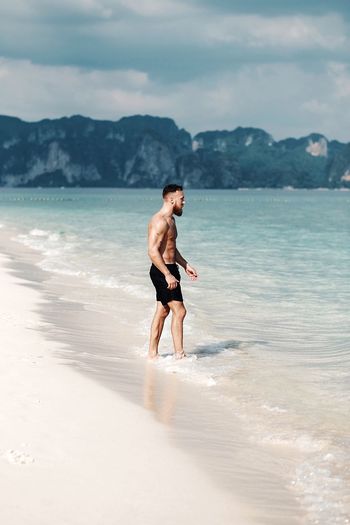 Side view of shirtless man standing in water at beach