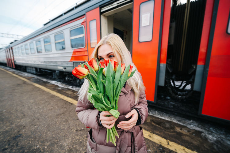 Girl at the train station next to the train covered her face with tulip flowers