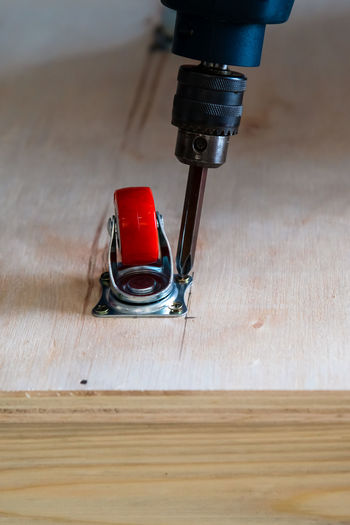 Close-up of electrical screwdriver fixing castor wheel on a wooden table.