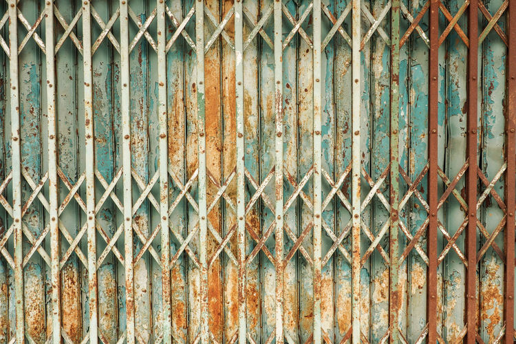 Full frame shot of rusty metal fence against wall