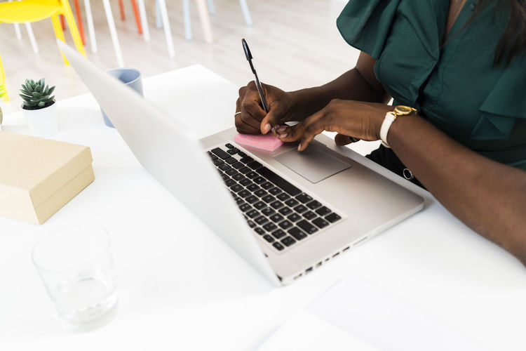 Businesswoman writing on adhesive note while working on laptop at office