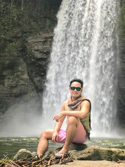 Man sitting on rock against waterfall