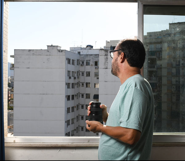 Middle-aged man looking out the window with an object in his hand