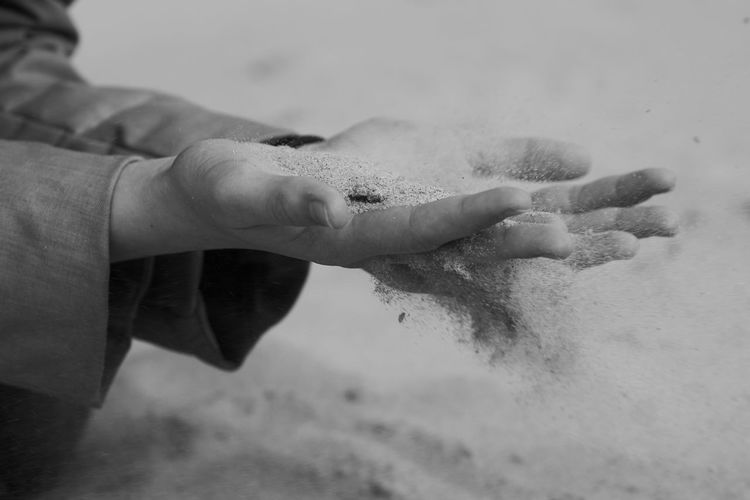 Cropped hands spilling sand at beach