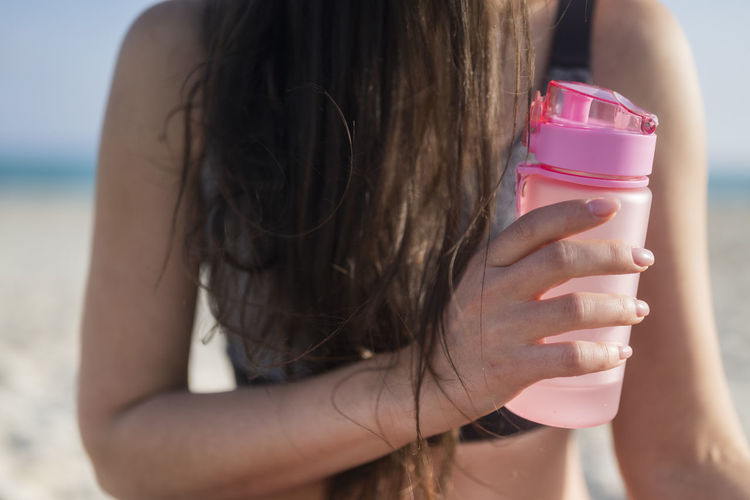 Midsection of woman drinking milk while standing at beach