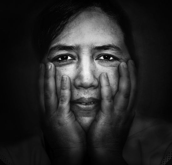 Close-up portrait of woman with head in hands against black background