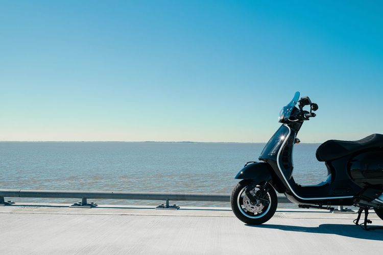 Rear view of man riding motor scooter on beach against clear blue sky