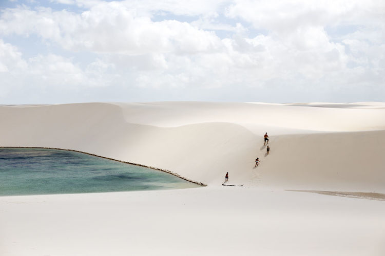 Rear view of people walking on sand dune by lake against sky