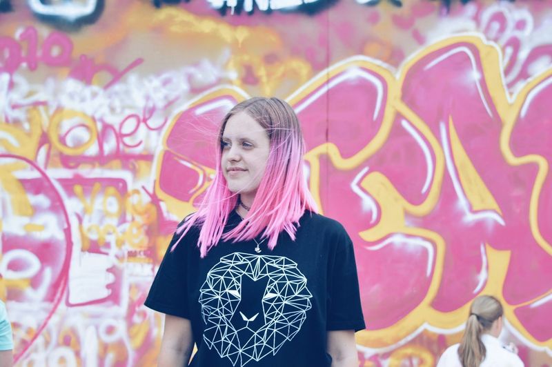 Full length of smiling young woman standing against graffiti