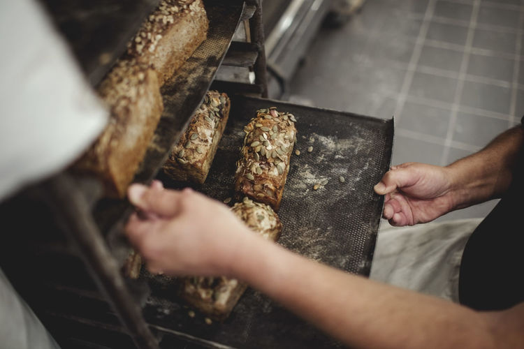 Midsection of baker holding fresh baked breads in tray on cooling rack at bakery