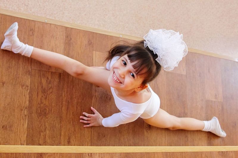 High angle portrait of cute girl stretching on hardwood floor