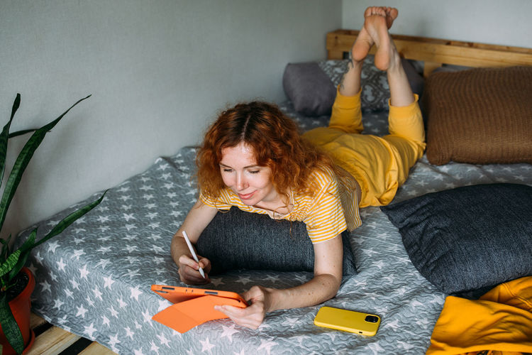 Portrait of young woman using mobile phone while lying on bed at home