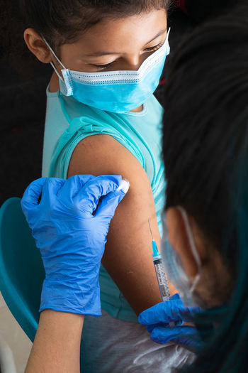 Children's nurse disinfecting brown girl's arm before administering injection.
