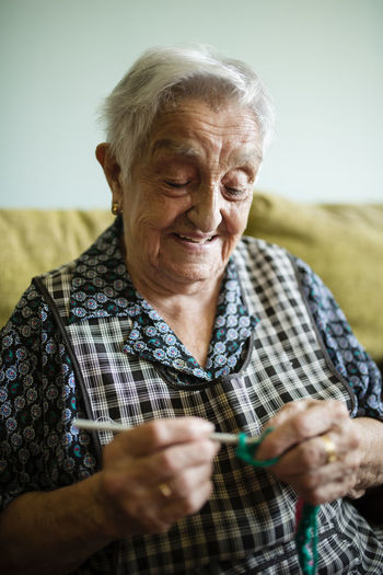 Portrait of smiling senior woman crocheting on the couch at home